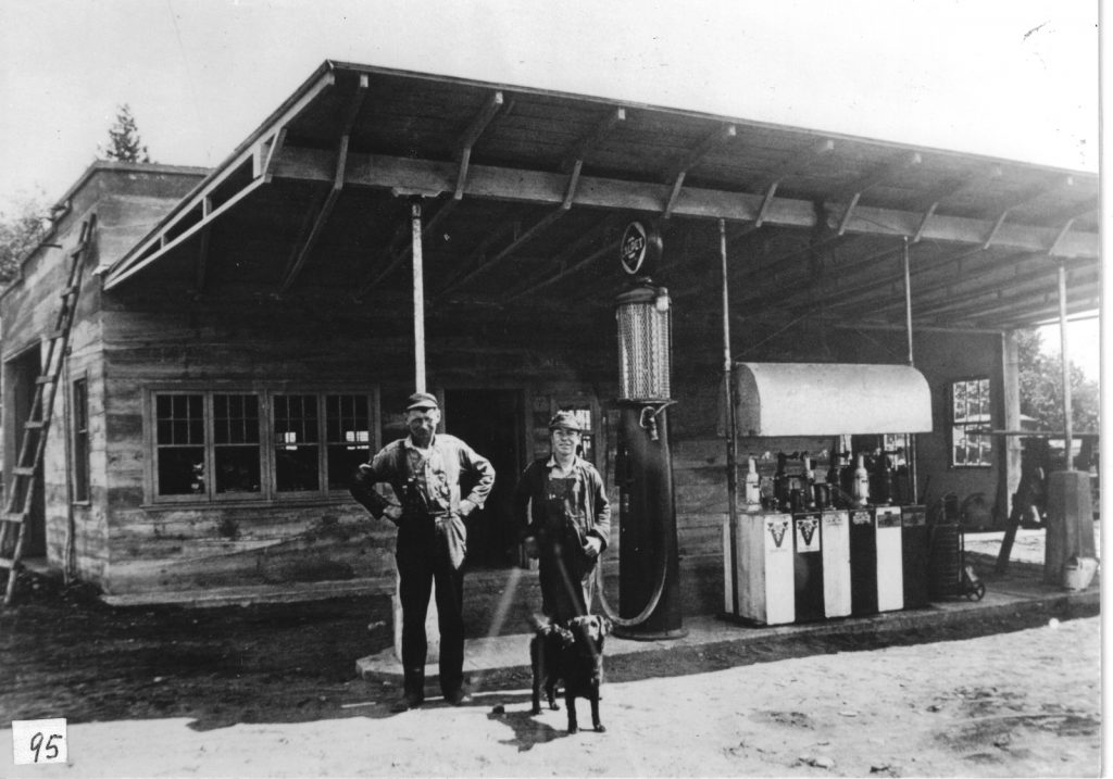 Two men and dog in front of old gas station